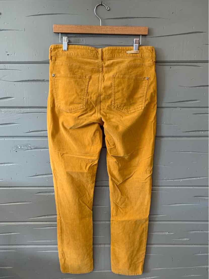 Mustard yellow slim-fit pants with five-pocket styling and belt loops hanging on wooden hanger.