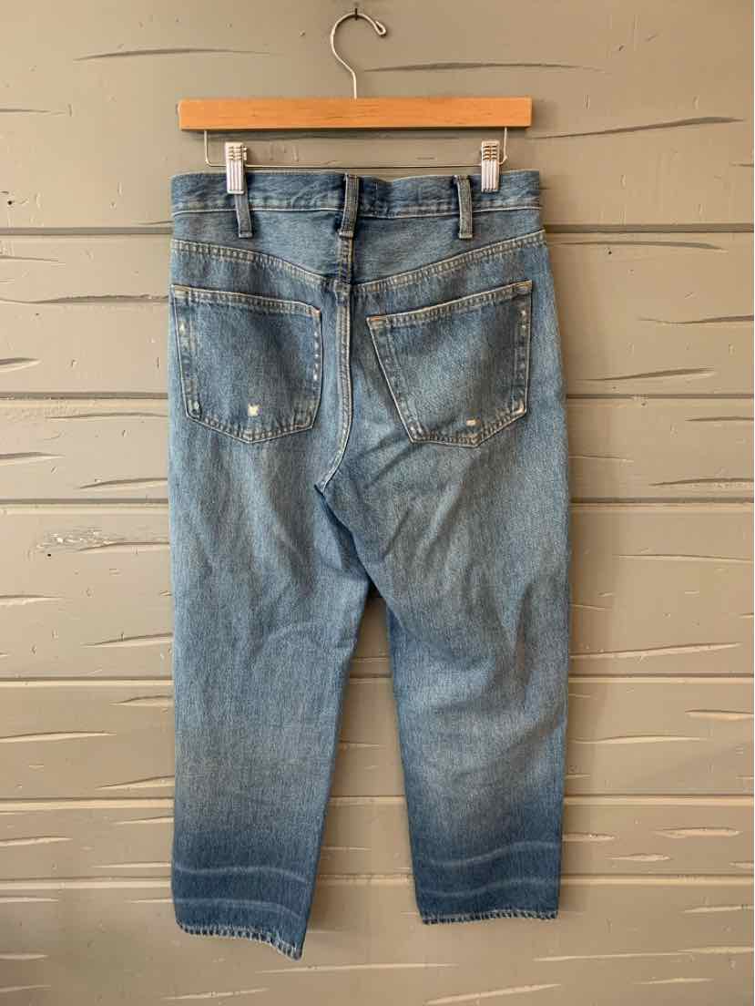 Light blue denim jeans with slight fading and distressed details, hanging by clips on wooden hanger.