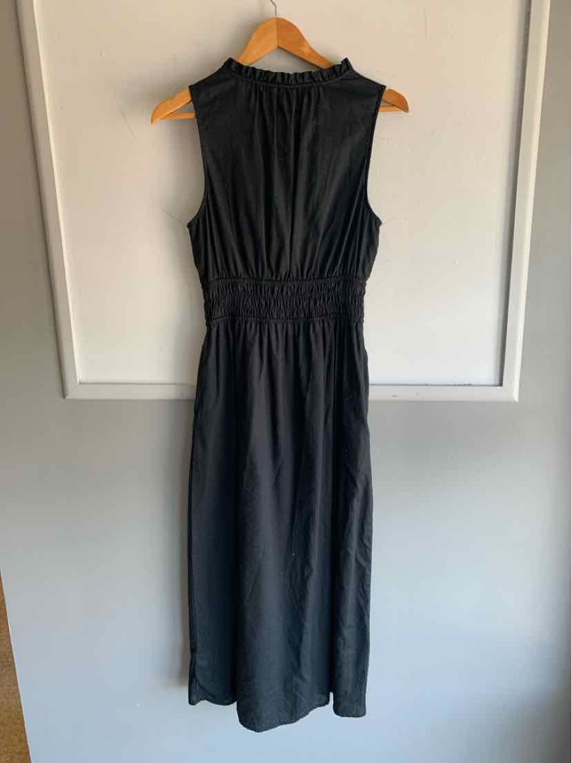 Sleeveless black midi dress with gathered waist and ruffled neckline hanging on wooden hanger.