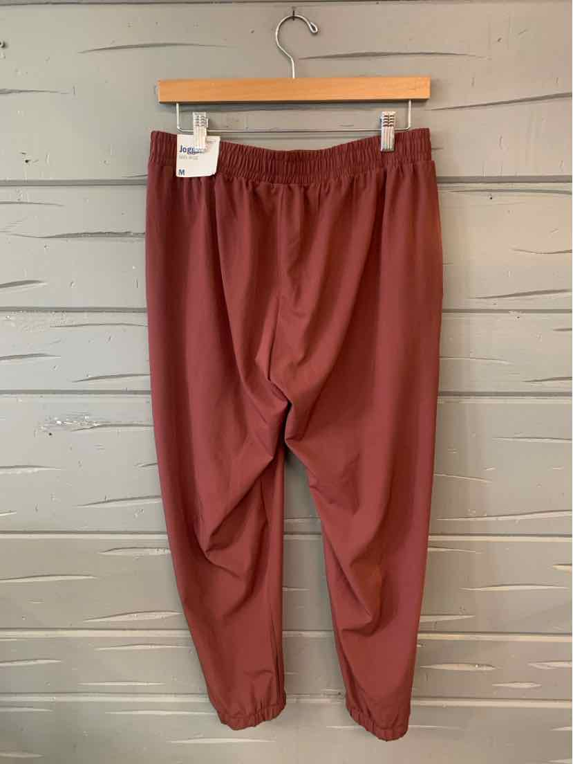 Brown elastic waist jogger pants with cuffed ankles hanging on wooden hanger.