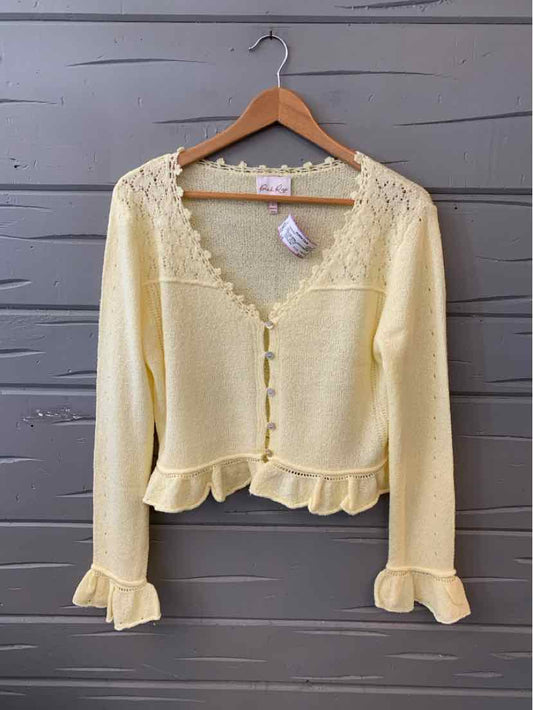 Light yellow knit cardigan with lace trim along neckline and chest, button-front and ruffled hem and cuffs.