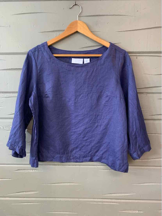 Blue linen long-sleeve top with scoop neck and relaxed fit hanging on wooden hanger.