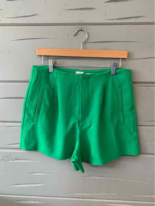 Bright green high-waist shorts with front patch pockets and a clean waistband hanging on wooden hanger.