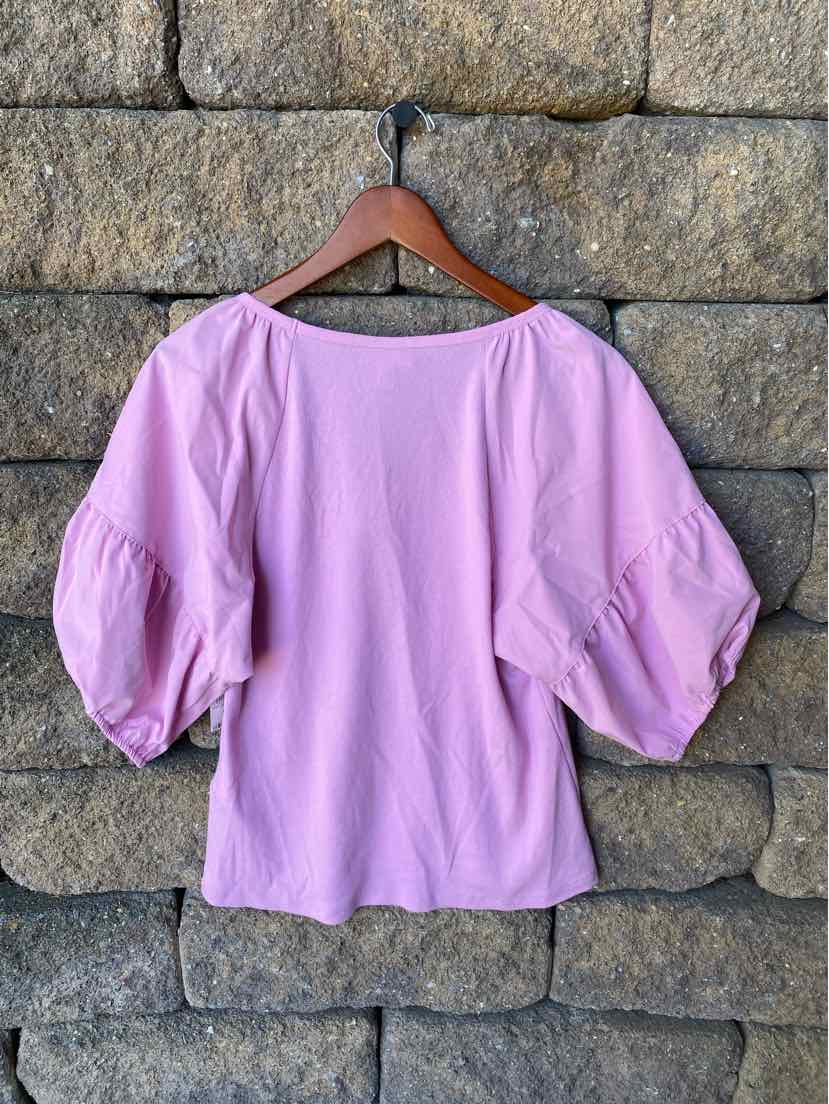 Light pink blouse with wide scoop neckline and voluminous puff sleeves hanging on wooden hanger.