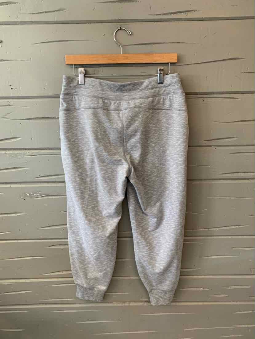 Heather gray cropped jogger pants with elastic cuffs and wide waistband on wooden hanger against gray wood panel wall.