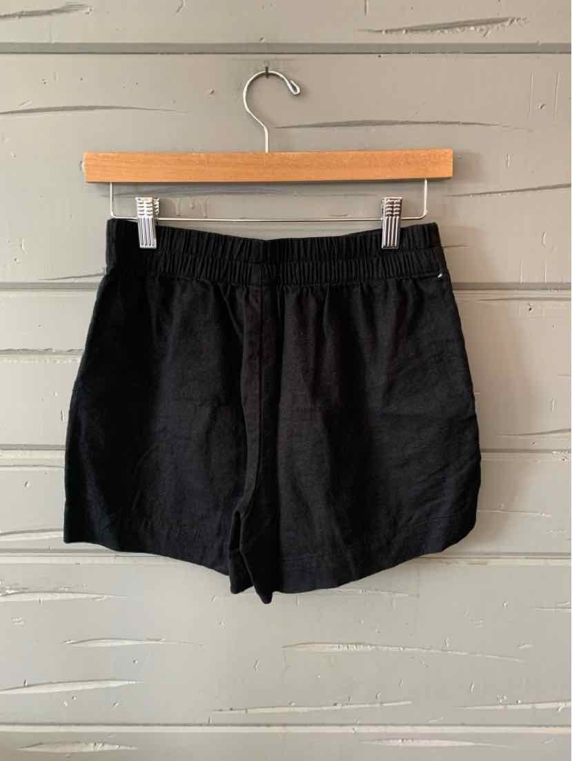 Black lightweight fabric shorts with elastic waistband and loose fit, hanging on wooden hanger.