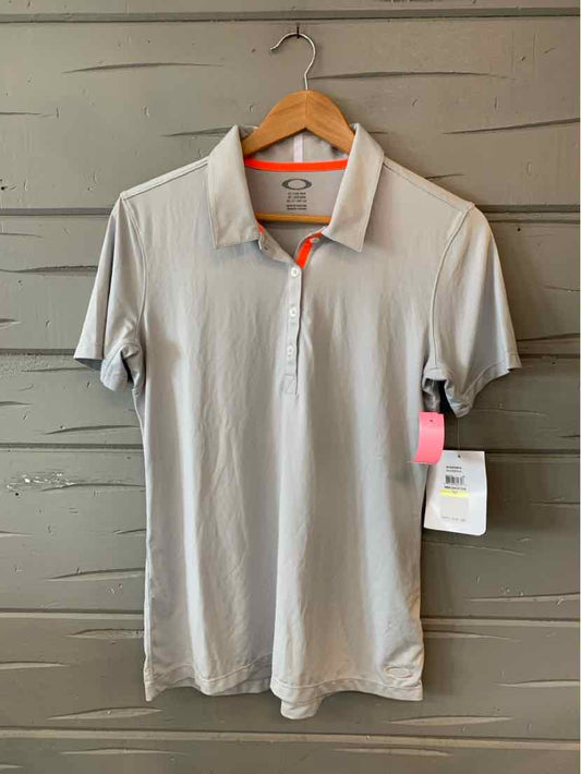 Light gray oakley polo shirt with short sleeves and a three-button placket on a wooden hanger.
