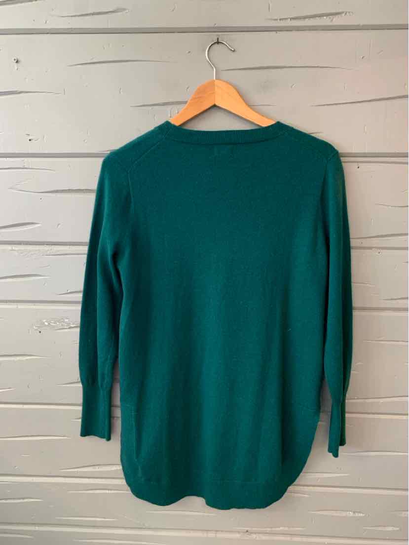 Teal green long-sleeve knit sweater with crew neckline and ribbed cuffs hanging on wooden hanger.