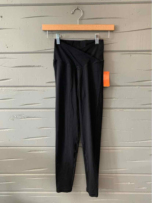 Black high-waisted leggings with a wide waistband and a tight, stretchy fit hanging on a wooden hanger against a gray.