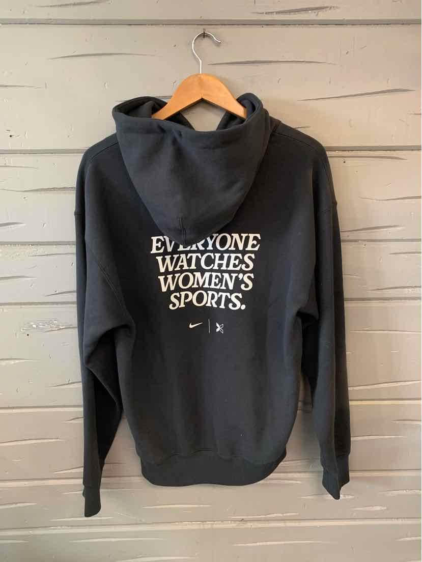 Black Nike hoodie with white "Everyone Watches Women's Sports" text and kangaroo pocket.