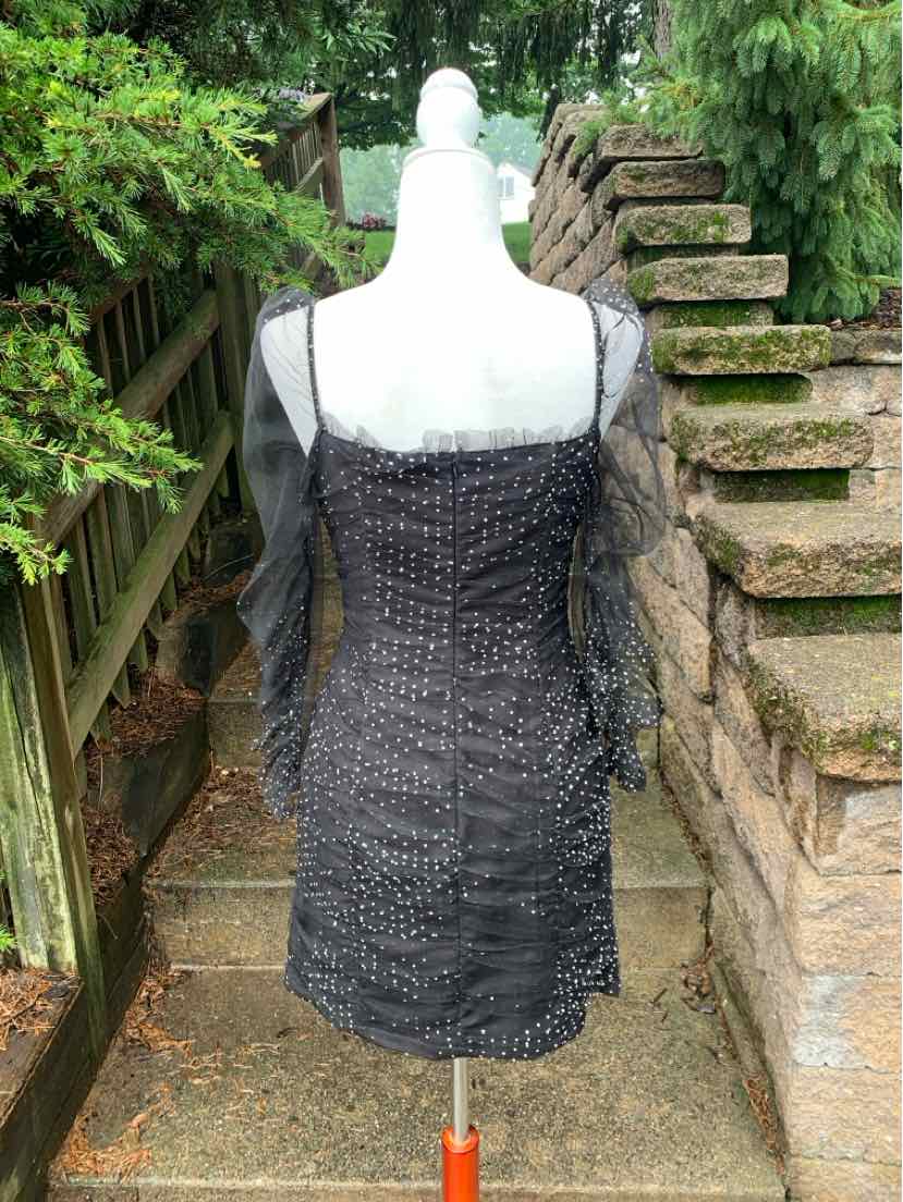 Black mini dress with sheer long sleeves and polka dot textured fabric, fitted silhouette.