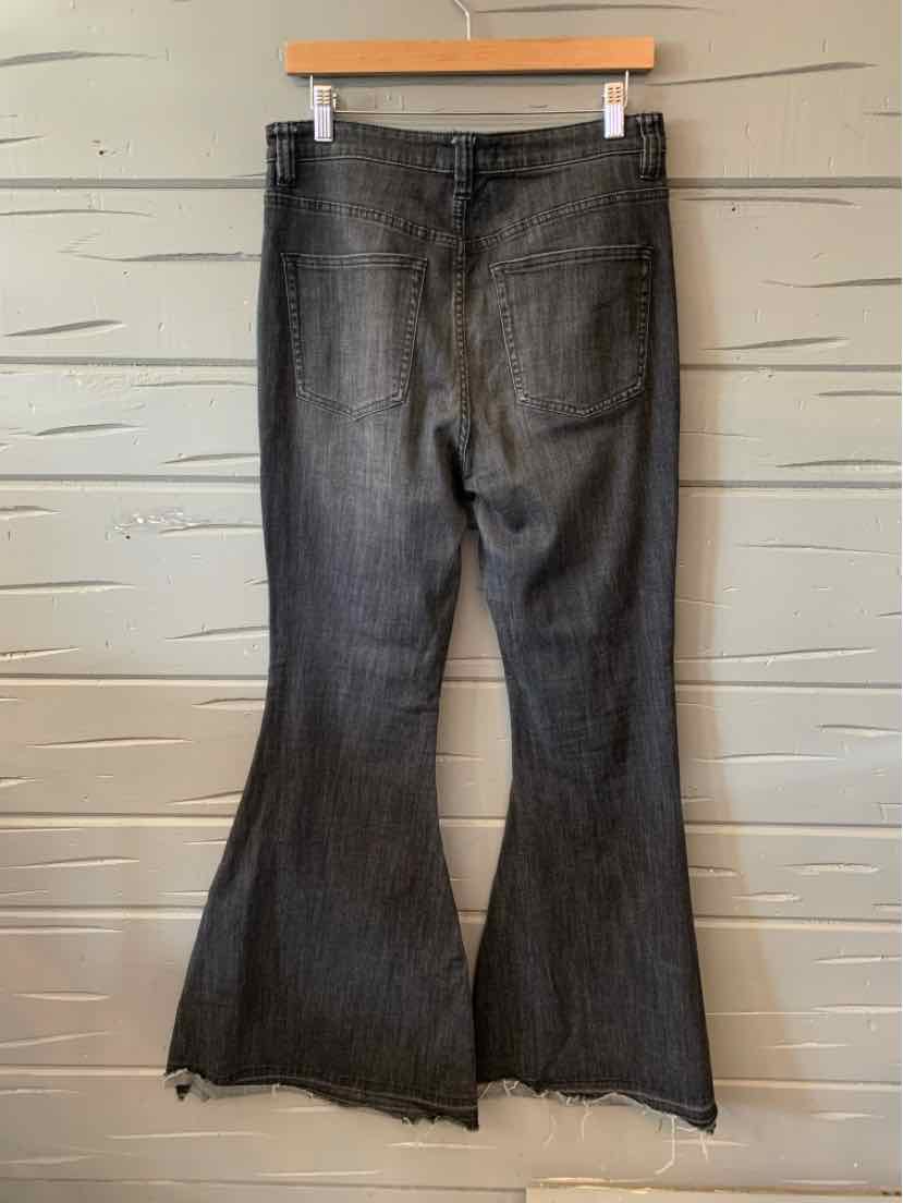 Black flared denim jeans with frayed hems hanging on wooden hanger against wooden background.