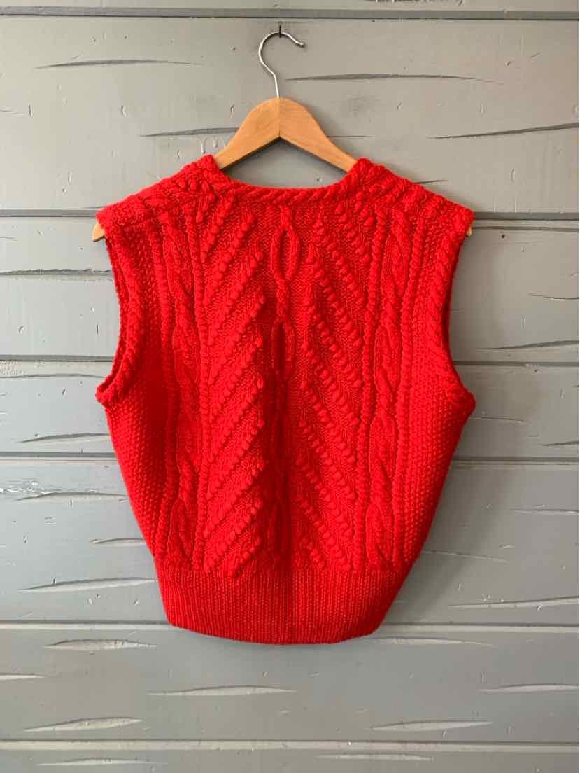 Bright red knitted sleeveless sweater vest with a cable-knit front and ribbed hem, hanging on a wooden hanger.