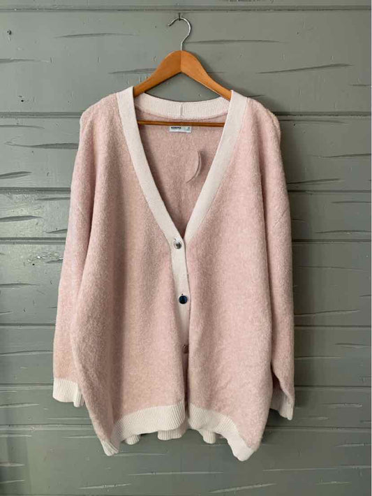 Light pink oversized cardigan with white trim and button closure hanging on wooden hanger.