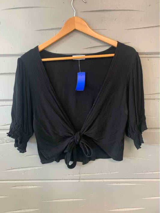 Black cropped blouse with deep V-neck, tie front, and ruched elbow-length sleeves on wooden hanger.