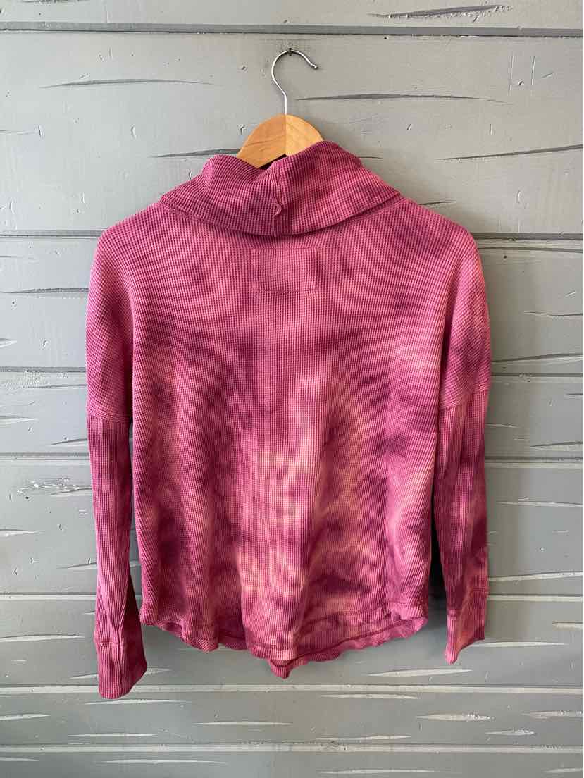 Long-sleeve pink tie-dyed top with high collar hanging on wooden hanger against gray wall.