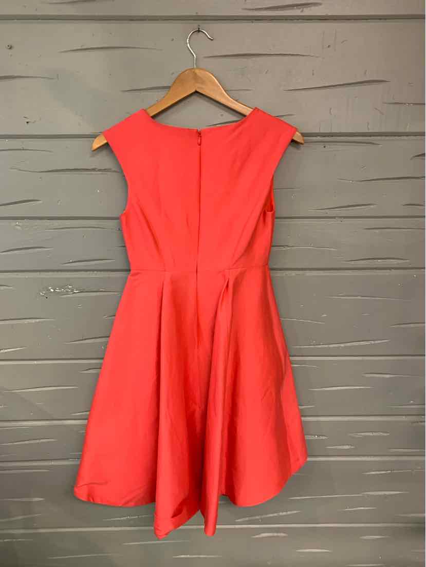 Coral pink sleeveless fit-and-flare dress with a round neckline and pleated skirt hanging on wooden hanger.