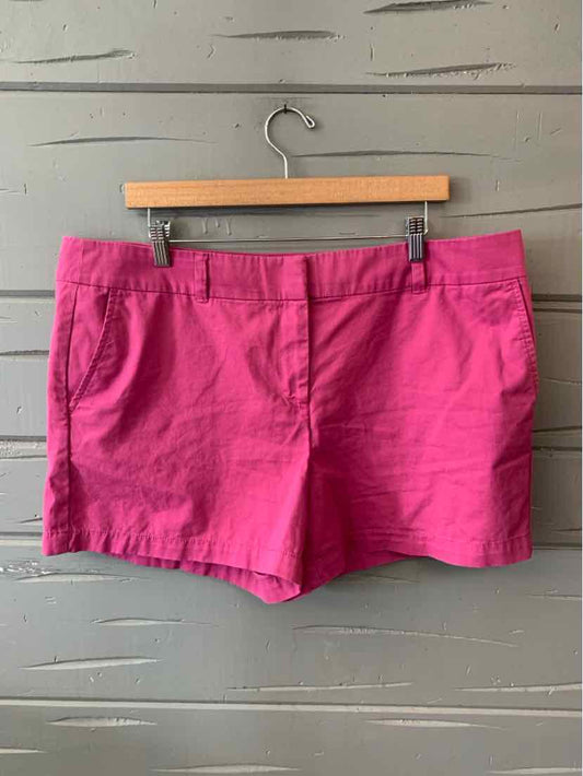 Bright pink cotton blend women's shorts with front pockets and belt loops hanging on wooden hanger.