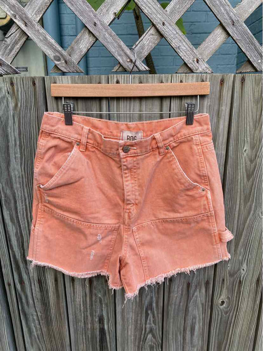 High-waist orange denim shorts with frayed hem and front pockets on wooden hanger.