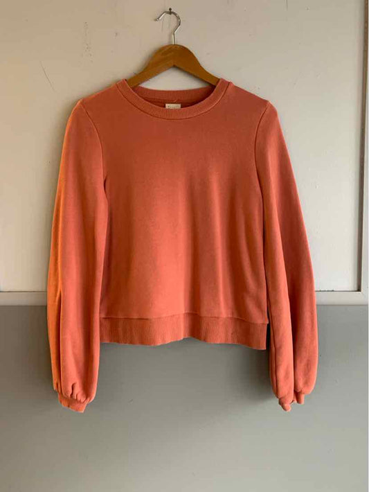 Orange long-sleeve crew neck sweater with ribbed cuffs and hem on wooden hanger.