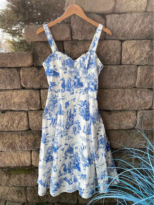 White dress with blue toile print, fitted bodice, adjustable straps, and flared skirt.