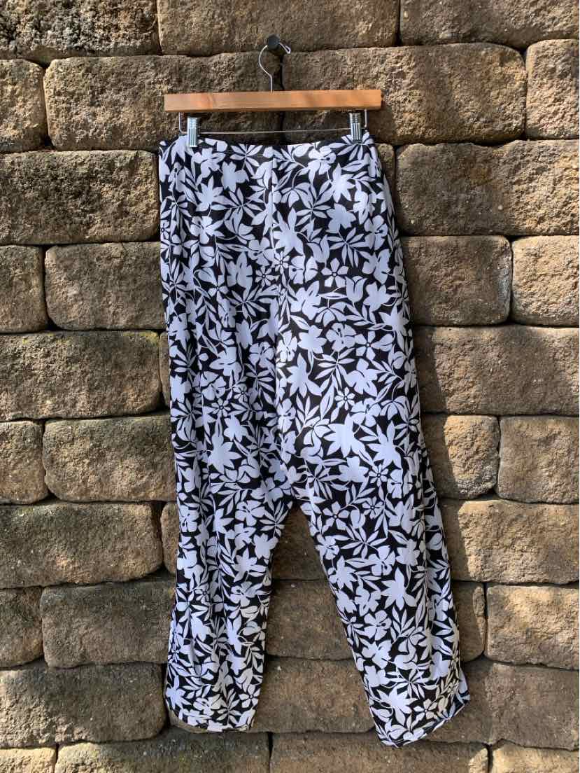 Black and white floral print casual pants with elasticized cuffs on hanger against stone wall background.