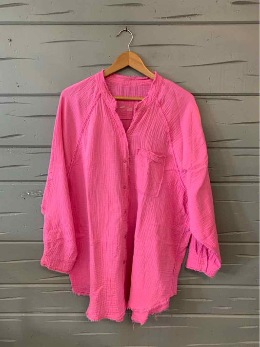 Pink long-sleeve blouse with button placket and gathered cuffs on wooden hanger.