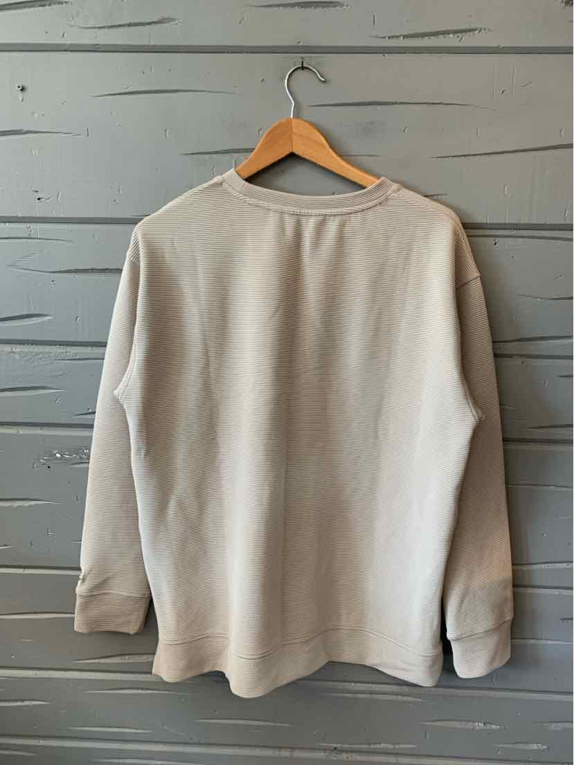Beige long-sleeve crew neck sweatshirt with ribbed cuffs and a relaxed fit hanging on wooden hanger.
