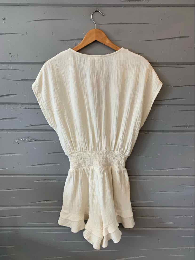 White short-sleeve romper with cinched waist and relaxed fit hanging on a wooden hanger.