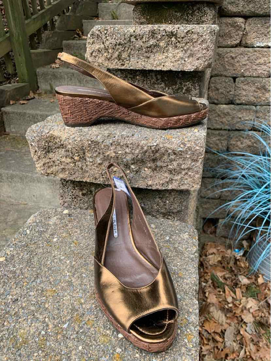 Bronze leather wedge sandals with peep toes and slingback straps on a textured stone surface.