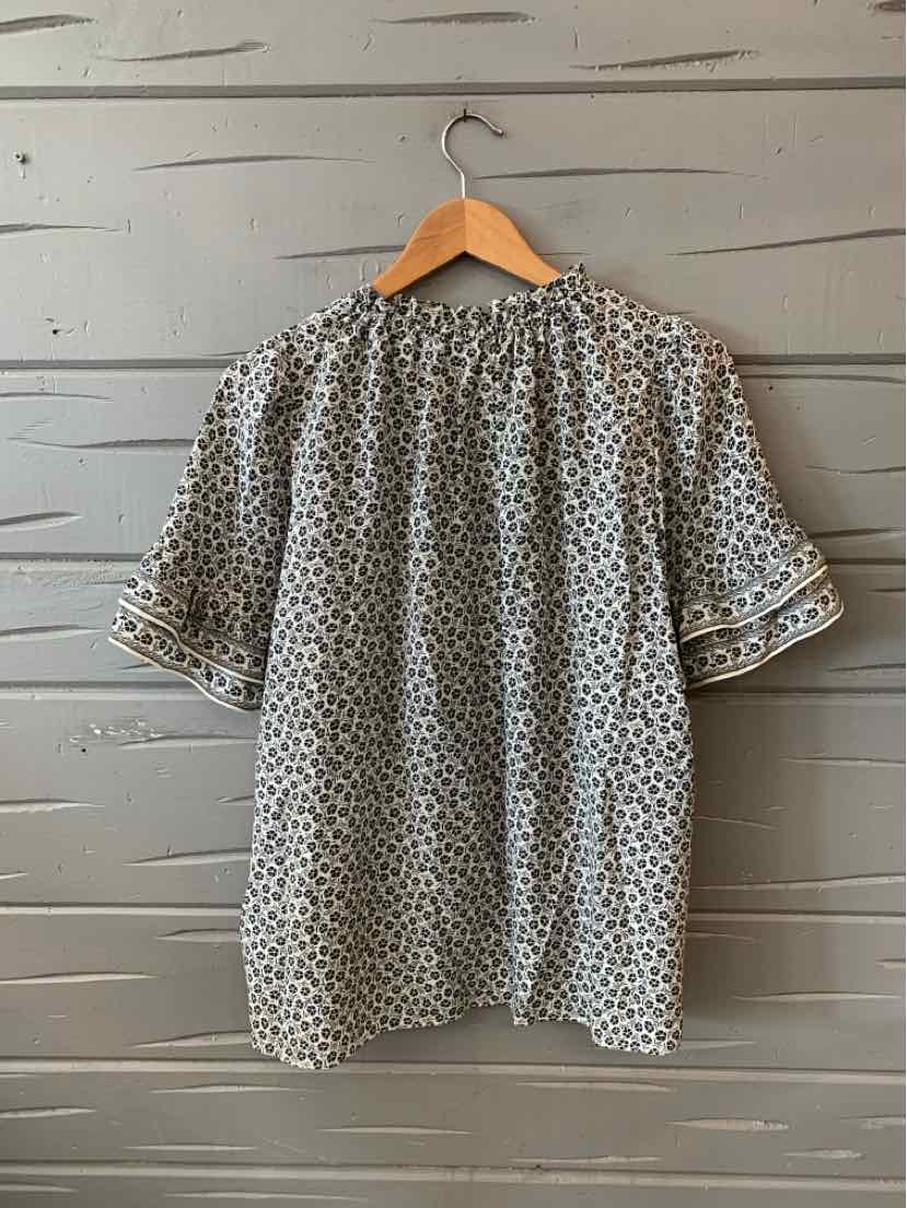 Black and white patterned short-sleeve blouse with relaxed fit hanging on wooden hanger.