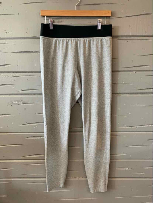 Light gray leggings with black elastic waistband hanging on wooden hanger against gray wooden wall.
