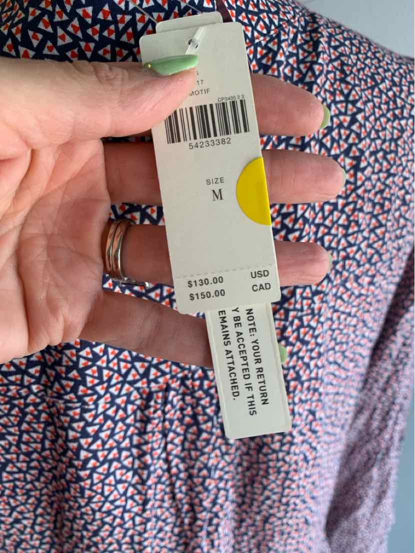 Hand holding a blue patterned garment with a white and yellow price tag showing size medium and prices in USD and CAD.