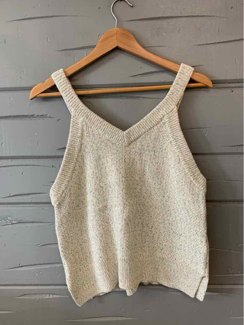 Cream knit sleeveless V-neck sweater top with wide straps on wooden hanger against gray wall.