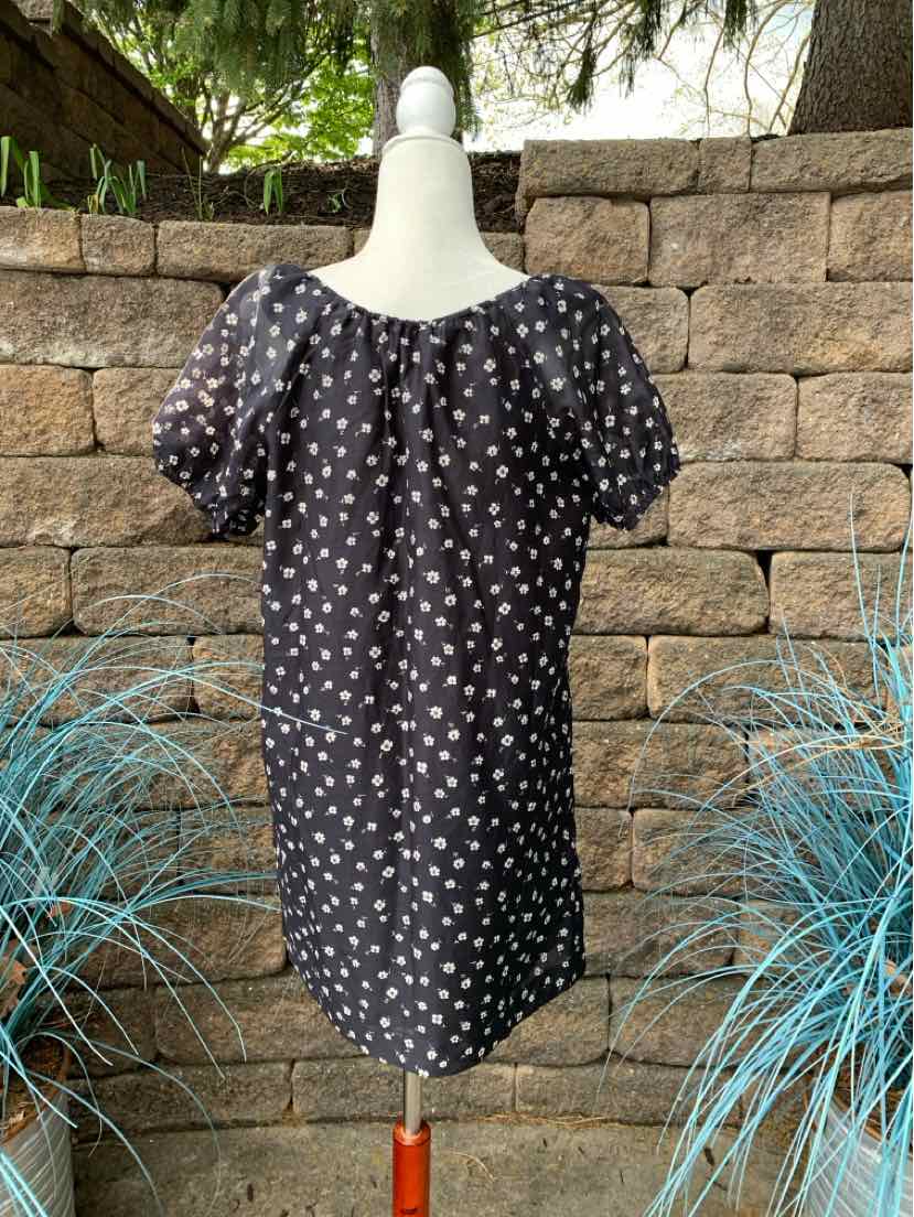 Black short-sleeve blouse with white floral print and gathered neckline on mannequin.