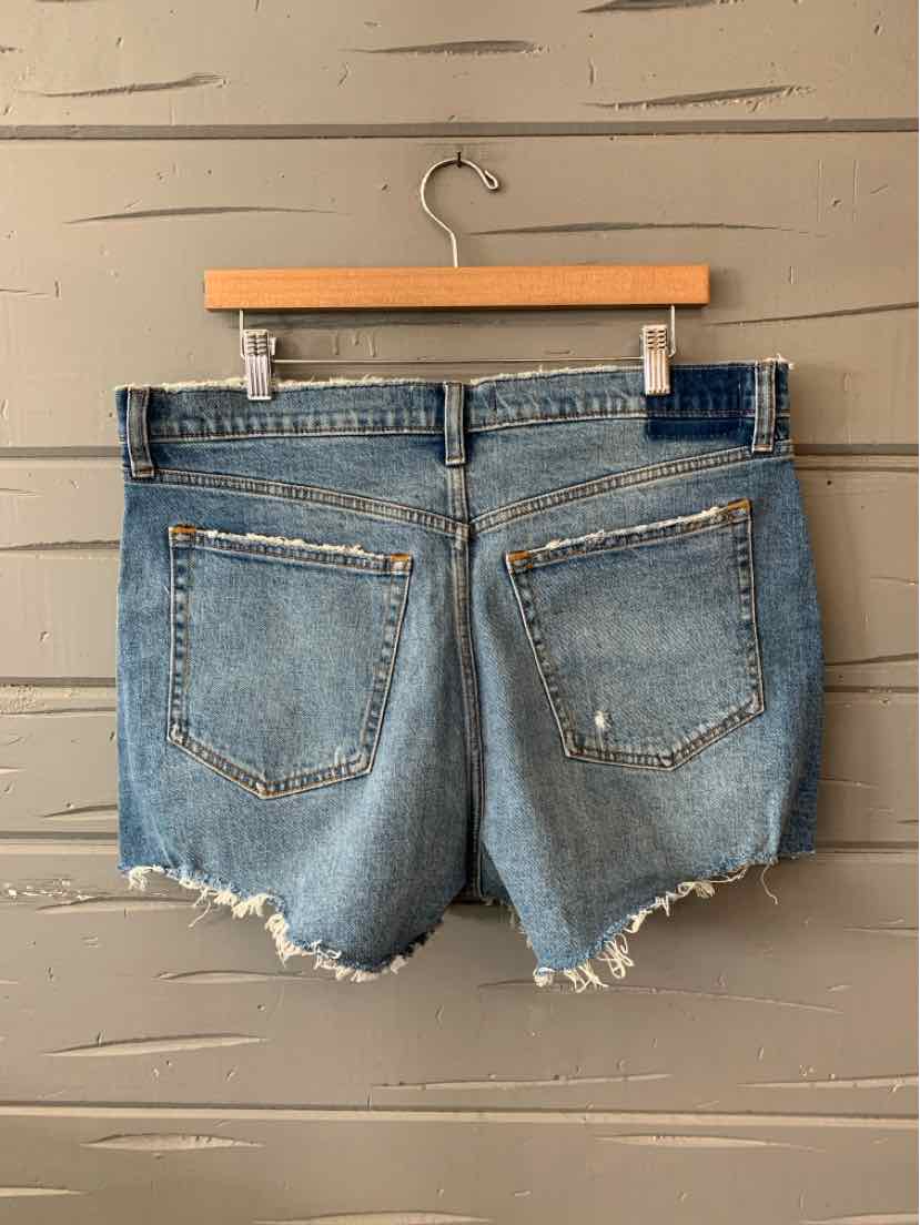 Light blue denim shorts with frayed hem and two back pockets hanging on wooden hanger.