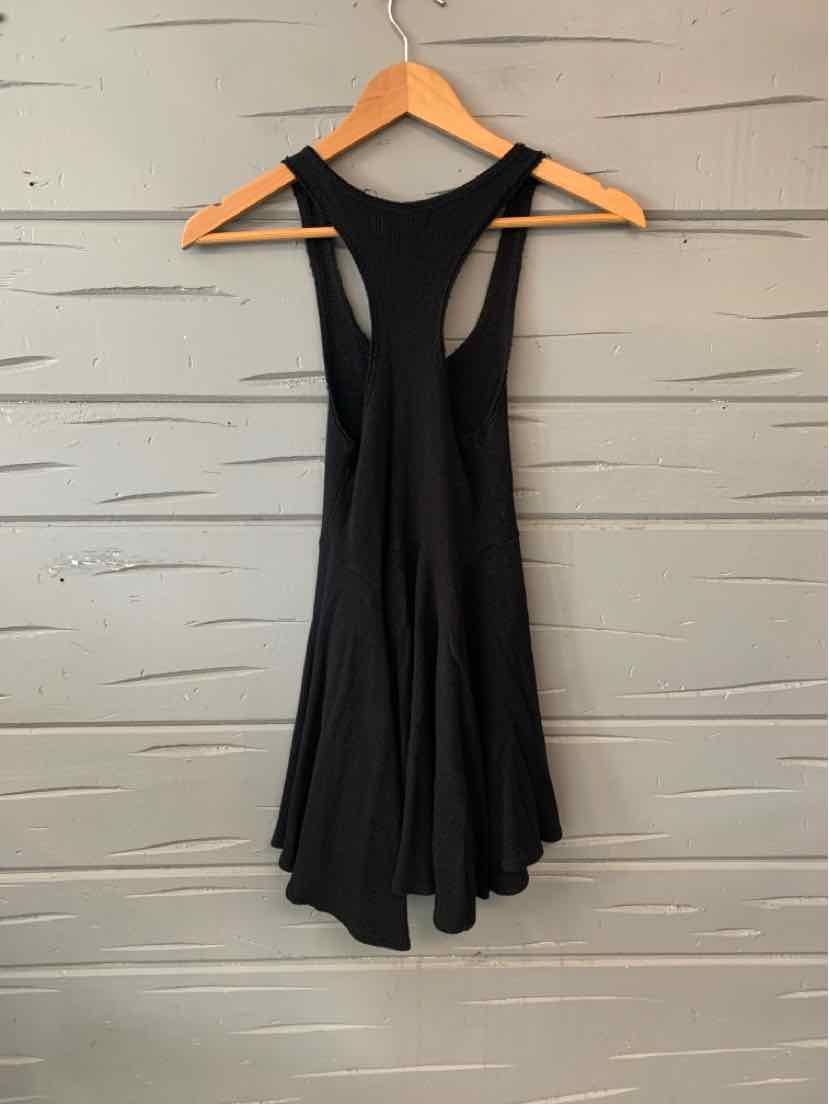 Black racerback tank top with flared hem, hanging on wooden hanger against textured wall.