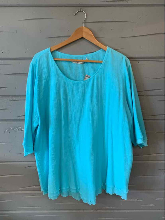 Light blue oversized scoop neck blouse with three-quarter sleeves and scalloped hem hanging on wooden hanger.