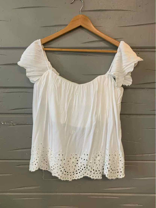 White eyelet cotton blouse with puff sleeves and scalloped hem hanging on wooden hanger.