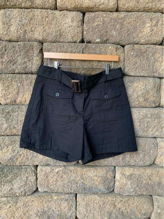 Black high-waist shorts with front pockets and belt loops hanging on wooden hanger against stone wall.