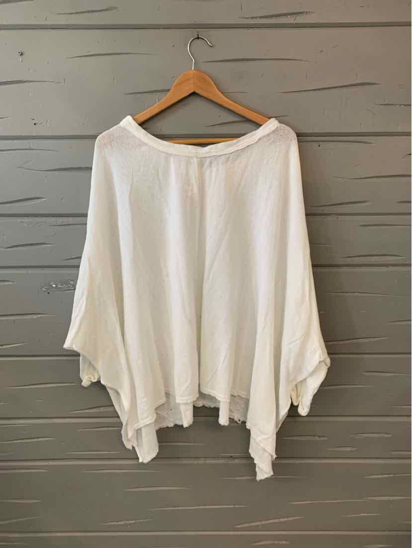 White loose-fitting long sleeve blouse with wide boat neckline and asymmetrical hem on wooden hanger.