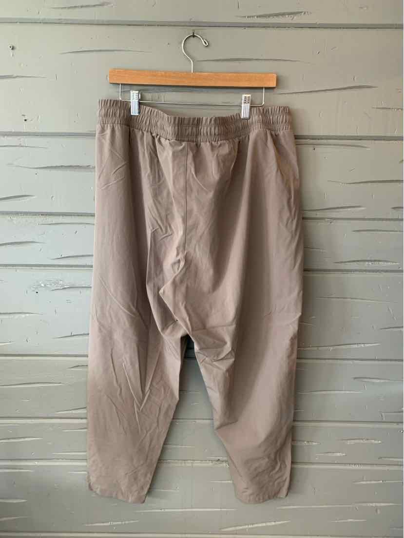 Beige relaxed-fit pants with elastic waistband and tapered legs hanging on wooden hanger.