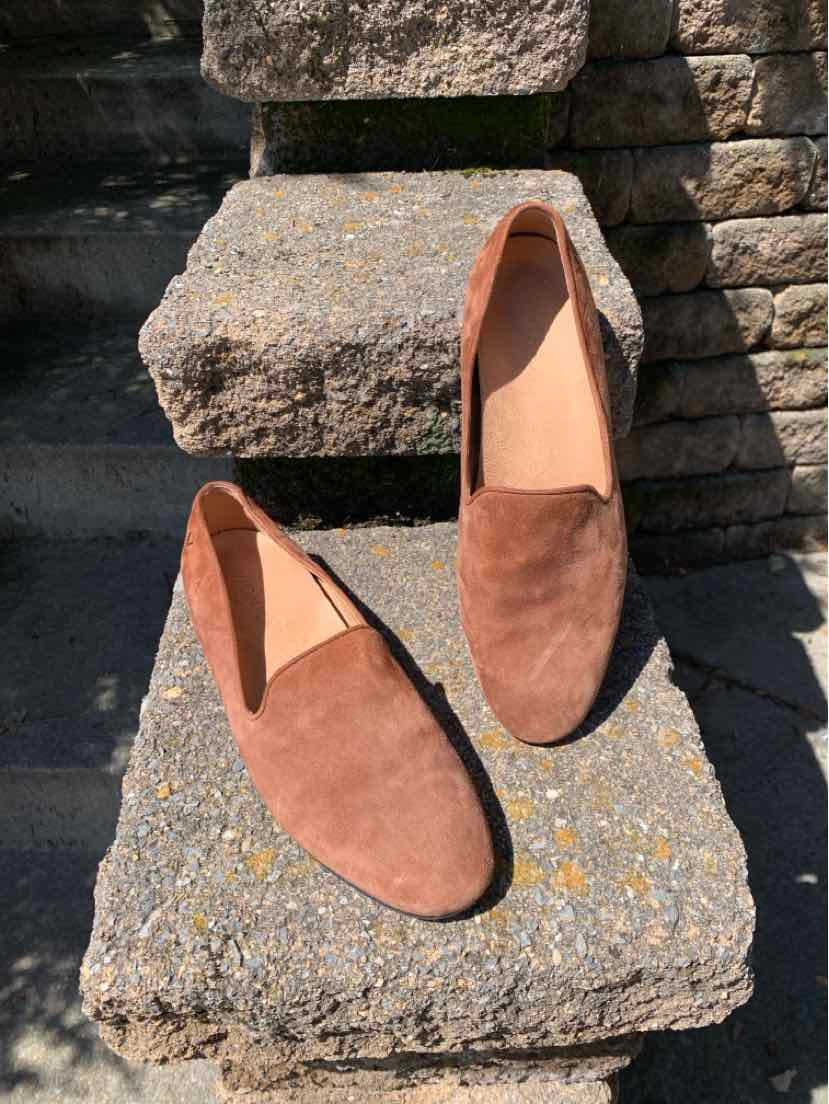 Brown suede slip-on shoes with rounded toes and minimalist design on stone steps.