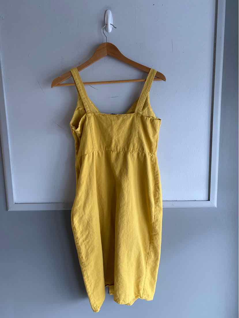 Yellow sleeveless midi dress with wide straps and gathered waist hanging on wooden hanger.