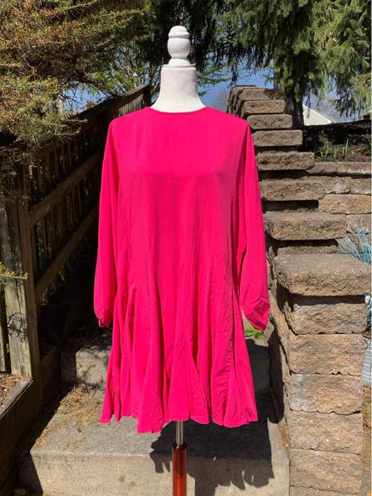 Bright pink long-sleeve dress with loose fit and round neckline on a mannequin outdoors.