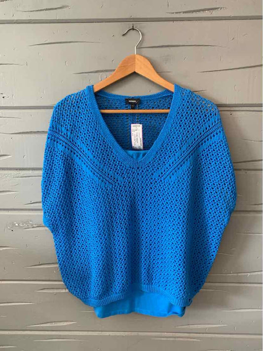 Bright blue knit sweater with V-neck and loose, relaxed fit hanging on wooden hanger against gray wall.