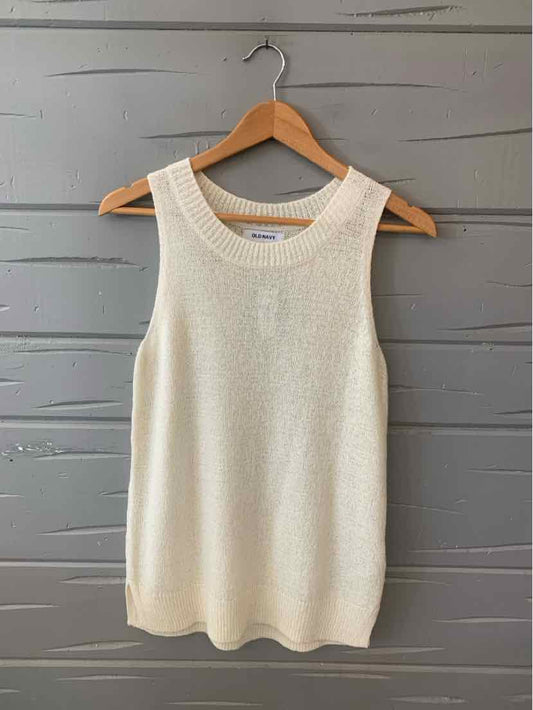 Cream-colored knit sleeveless top with round neckline on wooden hanger against gray wall.