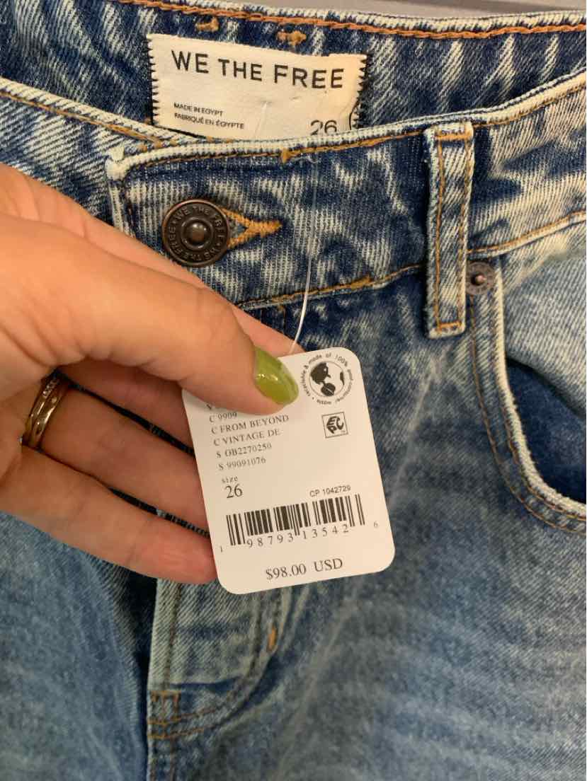 Light blue denim jeans with metal button closure, visible brand label, and size 26 tag held by hand.