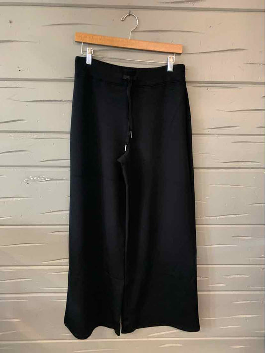 Black wide-leg pants with a high waist and smooth fabric hanging on a wooden hanger against a textured beige background.