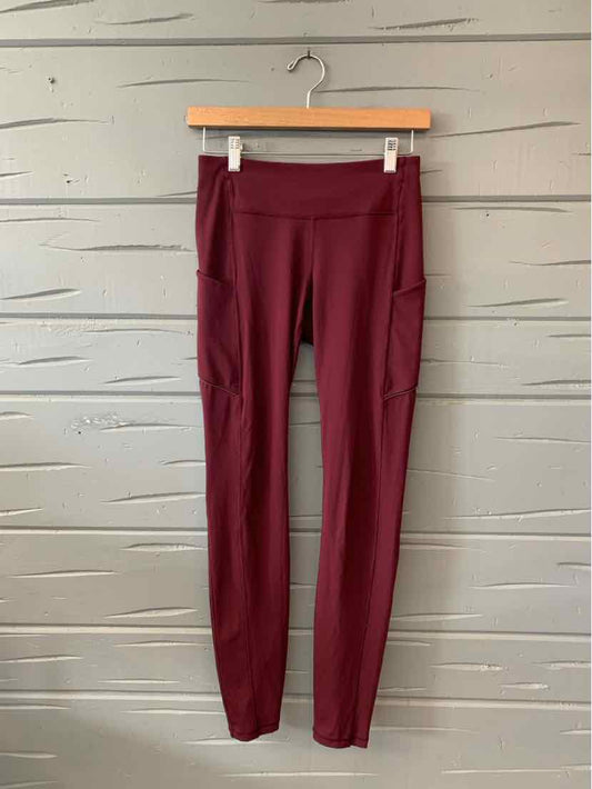 Burgundy high-waist leggings with side pockets and a slim fit hanging on a wooden hanger.